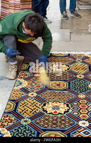 Ein Händler in Barkhor Square Pinsel reinigt seine Waren, einen traditionellen tibetischen, handgeknüpften Teppich, wenn potenzielle Kunden vorbeikommen. Stockfoto