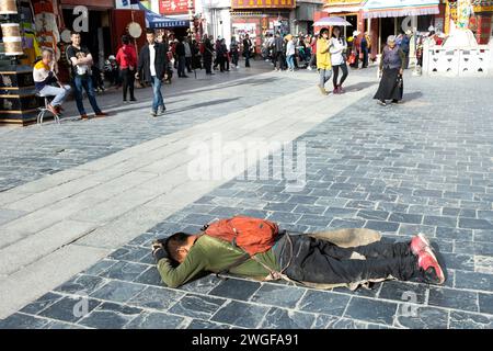 Ein Mann legt sich mit seinem Gesicht auf den Boden, um sich vor Buddha in der Bakhor Street in Lhasa zu verbeugen. Stockfoto