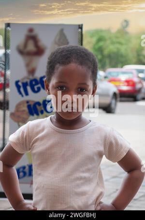 afrikanisches Mädchen, das auf der Straße steht, Einkaufszentrum mit Autos parkt Stockfoto