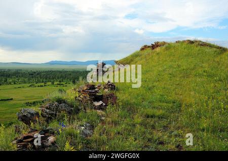 Geschichtete Felsformationen aus rotem Sandstein auf einem hohen Hügel mit Blick auf ein malerisches Tal an einem sonnigen Sommertag. Truhen in den Bergen, Khakassia, Stockfoto