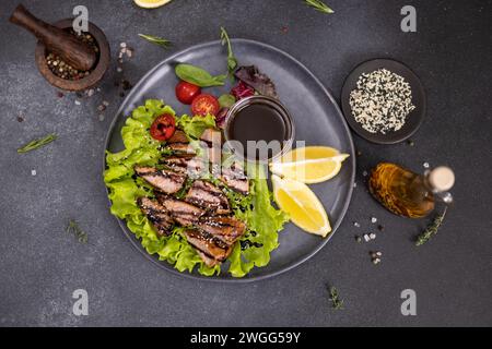 Stücke von gegrilltem Bio-Thunfisch auf schwarzem Keramikgericht mit Salat auf einem Tisch Stockfoto