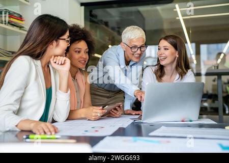 Lächelnd treffen sich verschiedene Kollegen in einem Brainstorming in der Vorstandsetage, um gemeinsam Finanzstatistiken zu diskutieren Stockfoto