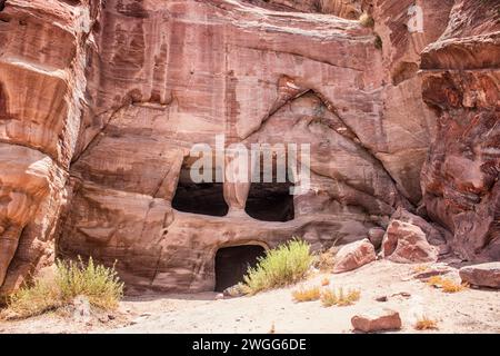 Vor einer Höhlenwohnung mit geschnitzter Tür und Fenstern im UNESCO-Weltkulturerbe. Petra ist eine historische und archäologische Stadt im Süden Jordaniens. Petra ist berühmt für seine Felsenarchitektur und das Wasserleitungssystem und wird wegen der Farbe des Sandsteins, aus dem es geschnitzt ist, auch „Rosenstadt“ genannt. Es grenzt an den Berg Jabal Al-Madbah, in einem Becken, das von Bergen umgeben ist, die die Ostflanke des Arabah-Tals bilden, das vom Toten Meer bis zum Golf von Aqaba verläuft. Der Zugang zur Stadt erfolgt über eine berühmte malerische Schlucht namens Siq, die direkt zum Khaz führt Stockfoto