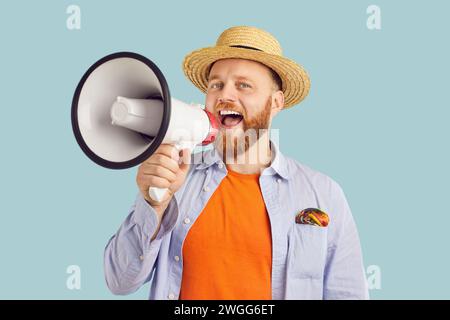 Junger bärtiger Mann in Sommerkleidung und Hut, der das Mundstück auf blauem Studiohintergrund hält. Stockfoto