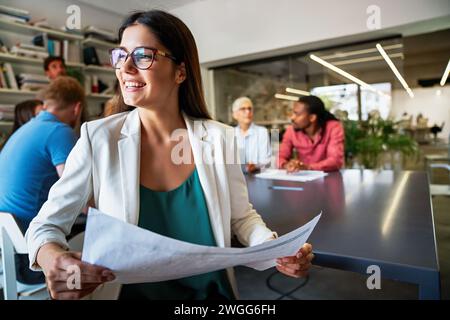 Lächelnd treffen sich verschiedene Kollegen in einem Brainstorming in der Vorstandsetage, um gemeinsam Finanzstatistiken zu diskutieren Stockfoto