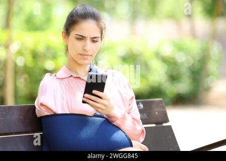 Besorgte Genesungsfrau, die auf einer Bank in einem Park das Telefon überprüft Stockfoto