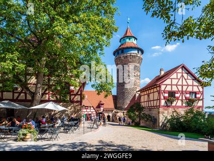 Touristen genießen den Innenhof der mittelalterlichen Kaiserburg in Nürnberg mit dem Tiefen Brunnen und dem Sinwellturm. Stockfoto