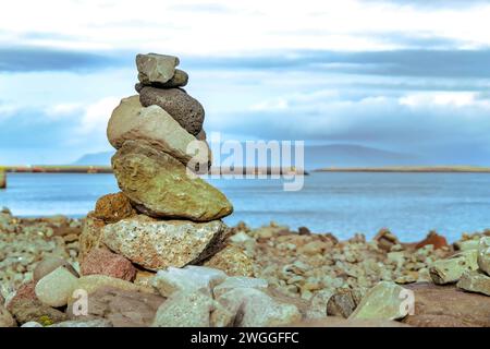 Kreatives Kunstwerk, in dem grobe, unebene Steine aufeinander gelegt werden, die sich am Meer mit felsigem Gelände gegen Wasser befinden Stockfoto