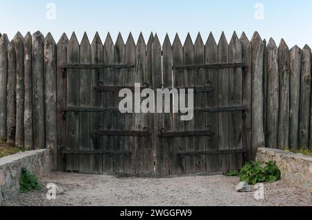 Alte Befestigungsstockade aus geschärften Stämmen und Holztoren mit geschmiedeten Scharnieren Stockfoto