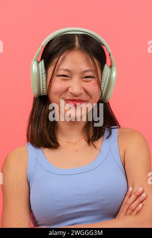 Vertikales Porträt junge lächelnde Chinesin isoliert auf rosa Hintergrund, Musik hören. Stockfoto