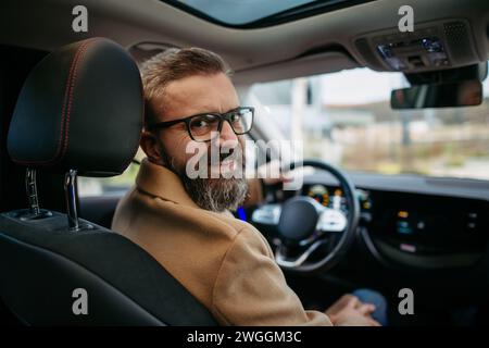 Porträt eines Reifen Mannes, der im Elektroauto sitzt und über die Schulter blickt. Stockfoto