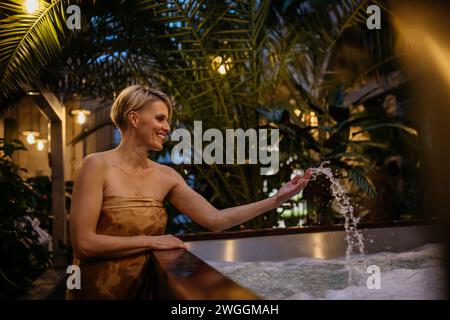 Schöne Frau, die am Whirlpool steht, Wasser spritzt, Wellness-Wochenende im Spa genießt. Stockfoto