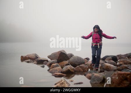 Eine Wanderer wandert entlang der felsigen Küste mit Blick auf einen nebelbedeckten Jordan Pond im Acadia-Nationalpark von Maine. Stockfoto