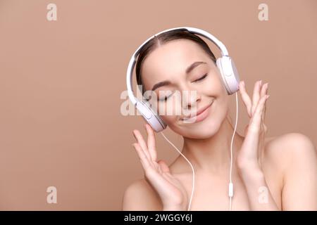 Eine hübsche junge Frau mit großen Kopfhörern genießt Musik. Isoliert auf beigefarbenem Hintergrund. Stockfoto