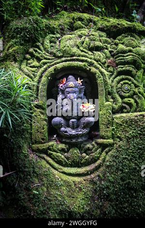 Schwarze Statue von Ganesha, in Nische gehauen auf Felsen bedeckt mit Moos Stockfoto