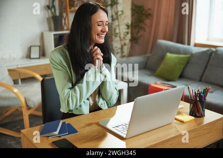 Junge Geschäftsfrau, die zu Hause mit einem Laptop sitzt, mit einem fröhlichen und aufgeregten Gesicht, die Reise online über Reiseservice Bucht Stockfoto