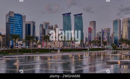 Skyline von Doha in der westlichen Bucht Doha, Katar Sonnenuntergang aus dem Hotelpark mit künstlichem See im Vordergrund und Wolken im Himmel im Hintergrund Stockfoto