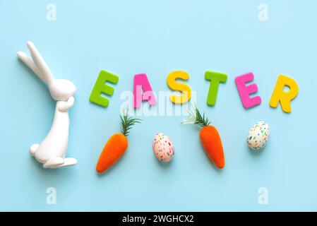 Frohe Ostern. Osterhase mit Karotten, ostereiern und farbigen Buchstaben mit dem Text ostern auf blauem Hintergrund Stockfoto