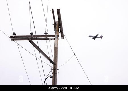 Manchester, New Hampshire, USA – Strommast mit Stromleitungen und vorbeifahrendem Flugzeug Stockfoto