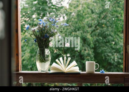 Ein Blumenstrauß und ein Buch auf der Fensterbank in einem gemütlichen Zuhause. Stockfoto