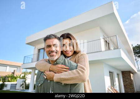 Glückliches lächelndes reifes älteres Familienpaar, neue Hausbesitzer stehen vor dem Haus. Stockfoto