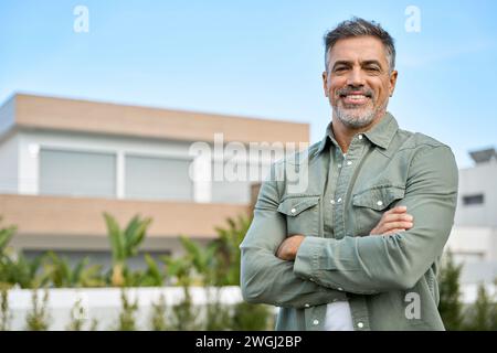 Glücklicher reifer Mann, neuer Eigentümer oder Makler, der vor dem Landhaus steht. Stockfoto