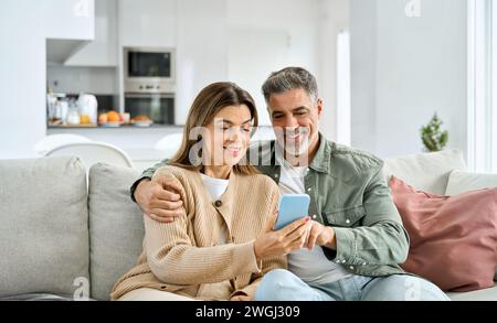Glückliches älteres Ehepaar, das das Smartphone benutzt und zu Hause entspannt auf der Couch sitzt. Stockfoto
