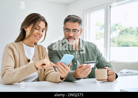 Glückliches Paar mittleren Alters, das ein Smartphone nutzt und eine Kreditkarte online kauft. Stockfoto