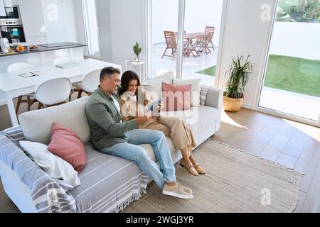 Glückliches reifes, altes Paar, das sich zu Hause auf dem Sofa umarmt und ein digitales Tablet verwendet. Stockfoto