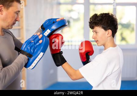 Teenager mit Boxhandschuhen Übung und Schlag auf die Pads für das Boxen. Junge mit ihrem Trainer Vater im Fitnessstudio Stockfoto
