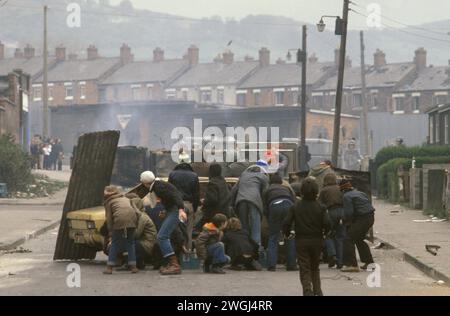 1980s die Probleme. Belfast entführte ein Auto, das von jungen IRA-Teenagern in Brand gesetzt wurde und als Barrikade im Benzinbombenkampf gegen die britische Armee im Hintergrund eingesetzt wurde. Etna Drive, Ardoyne Nord Belfast Großbritannien Nordirland HOMER SYKES Stockfoto