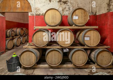 Holzfässer für die Weinreifung befinden sich auf drei Ebenen in einem toskanischen Keller Stockfoto