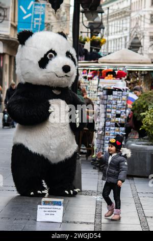 Eine riesige Panda-Figur vor Geschäften und Restaurants in der Fußgängerzone der Stadt, mit einem aufregenden kleinen Mädchen, das mit Panda fotografieren möchte. Stockfoto