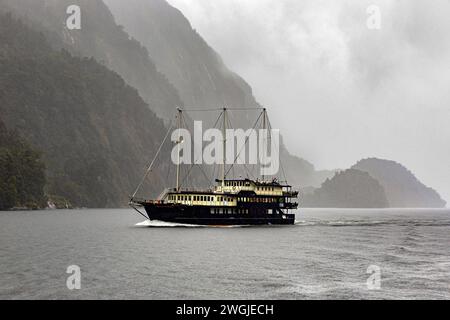 Touristenkreuzschiff, das an einem regnerischen Tag in Doubtful Sound / Patea, Fiordland / Te Rua-o-te-Moko, Neuseeland / Aotearoa, Südinsel / Te Waipoun weicht Stockfoto