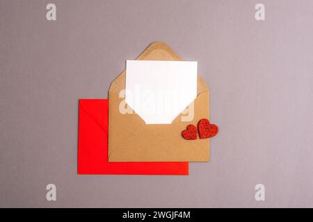 Umschlag mit leerer Karte und roten Herzen auf grauem Hintergrund. Valentinstag-Konzept, Draufsicht, flache Ladefläche, Mockup. Stockfoto