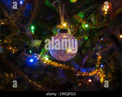Weihnachtskugel mit schönen Reflexen zwischen den bunten Lichtern eines Weihnachtsbaums. Weihnachtsdekoration. Stockfoto