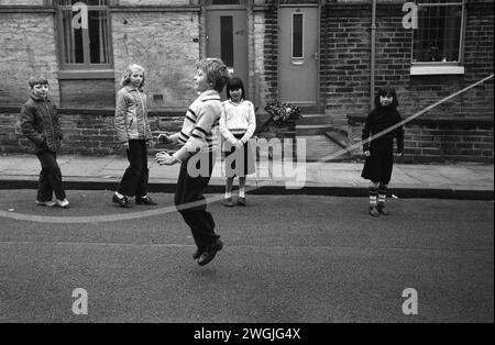 Großbritannien der 1980er Jahre, Kinder spielen zusammen, springen auf der Straße mit einem langen Sprungseil. Keine Autos. Saltaire war ein Modelldorf, dessen Bewohner in der Salts Mill arbeiteten, benannt nach Sir Titus Salt. Saltaire, Nr Bradford, West Yorkshire England 1981 HOMER SYKES Stockfoto