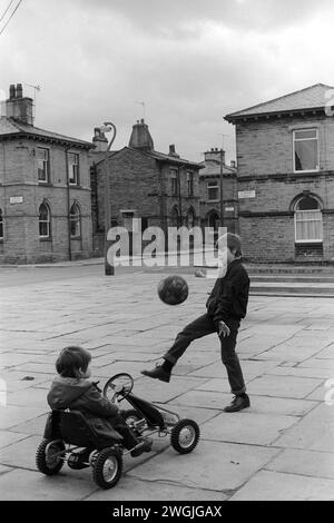 Saltaire Village Yorkshire. Kinder spielen zusammen, ein Junge in seinem Go-Kart, der andere tritt einen Fußball in den 1980er Jahren UK. Saltaire war ein Modelldorf, dessen Bewohner in der Salts Mill arbeiteten, benannt nach Sir Titus Salt. Saltaire, Nr Bradford, West Yorkshire England 1981 UNESCO-Weltkulturerbe HOMER SYKES Stockfoto