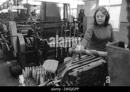 Junge Frau, die in der Textilindustrie in Salts Mill, West Yorkshire arbeitet. 1980er Jahre Großbritannien. Sie trägt Gehörschutz. Bei der Arbeit in der Fabrik war der Lärm lautstark. Salts Mill eine Baumwollfabrik, benannt nach Sir Titus Salt, wurde 1986 nach 133 Jahren als Textilfabrik geschlossen. England HOMER SYKES Stockfoto