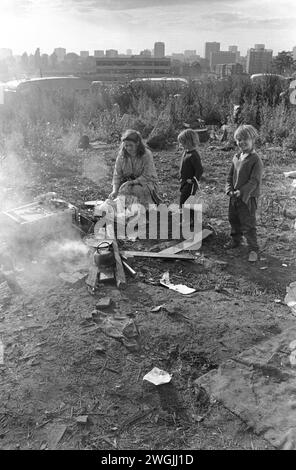 1960er Jahre Gypsey Mutter mit Kindern kocht eine Mahlzeit auf einem offenen Feuer Balsall Heath. Lager für irische Reisende. Stadtzentrum von Birmingham am Horizont. Die Wohnwagen der Reisenden zeigen sich. 1968 Birmingham England Großbritannien HOMER SYKES Stockfoto