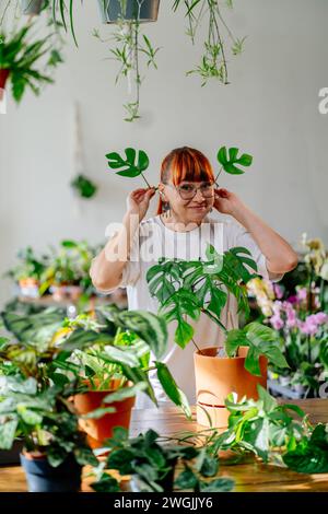 Gartenarbeiter, die Pflanzen pflegen. Millennials Gärtnerin hält eine junge Pflanze zwei Monsterablätter als Ohren. Konzept für Gartenanlagen Stockfoto