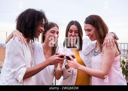 Vorderansicht von vier multiethnischen Freundinnen, die im Freien feiern und mit Rotwein anstoßen. Stockfoto