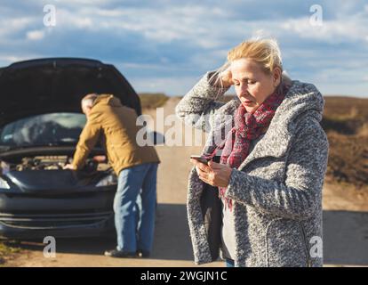 Eine ältere Frau auf der Straße hat einen Motorausfall, sie ruft um Hilfe. Stockfoto