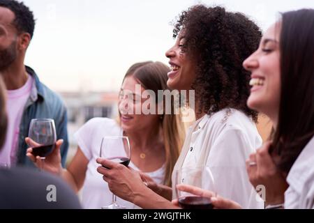 Freunde, die Spaß auf einer Terrasse haben, lachen, reden und Rotwein trinken. Stockfoto