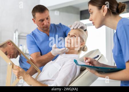 Männliche Kosmetikerin berät Frau mit Spiegel in der ästhetischen Klinik Stockfoto