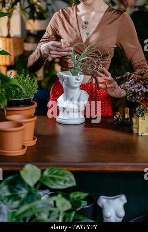 Vertikale Aufnahme einer kaukasischen Assistentin, die mit sukkulenter Pflanze ohne Boden im modernen Topf im Blumenladen arbeitet. Stockfoto