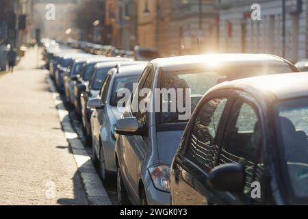 Panoramablick auf die Sonne, geparkte Autos auf der belebten Stadtstraße in der europäischen Stadt. Parken auf dem Gehweg, parallel zur Seite, voller Fahrzeuge, Stau im Stadtzentrum Stockfoto
