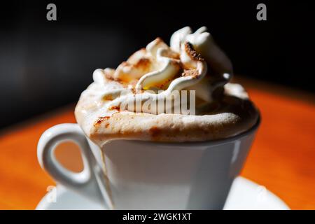 Cappuccino mit Schlagsahne in einer weißen Tasse auf einem Holztisch Stockfoto