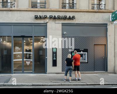 Straßburg, Frankreich - 2. Juli 2023: Ein Paar steht vor der Bankfiliale von BNP Paribas, die sich auf die Nutzung des Geldautomaten konzentriert Stockfoto