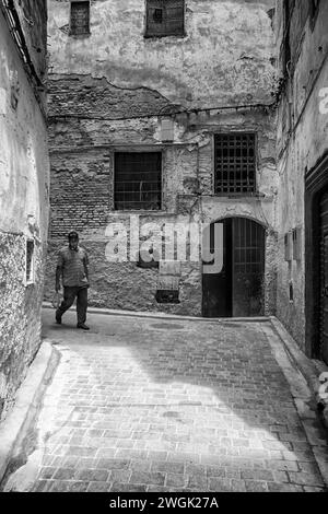Ein Mann, der durch die engen Medina-Gassen von Fès läuft. Fès, die zweitgrößte Stadt Marokkos, wird oft als Kulturhauptstadt des Landes bezeichnet. Es ist vor allem bekannt für seine von Fes El Bali ummauerte Medina mit mittelalterlicher marinidischer Architektur, pulsierenden Souks und der Atmosphäre der alten Welt. Die Medina beherbergt religiöse Schulen wie die Bou Inania aus dem 14. Jahrhundert und Al Attarine, die beide mit aufwändigen Zedernschnitzereien und kunstvollen Fliesen verziert sind. Marokko. Stockfoto